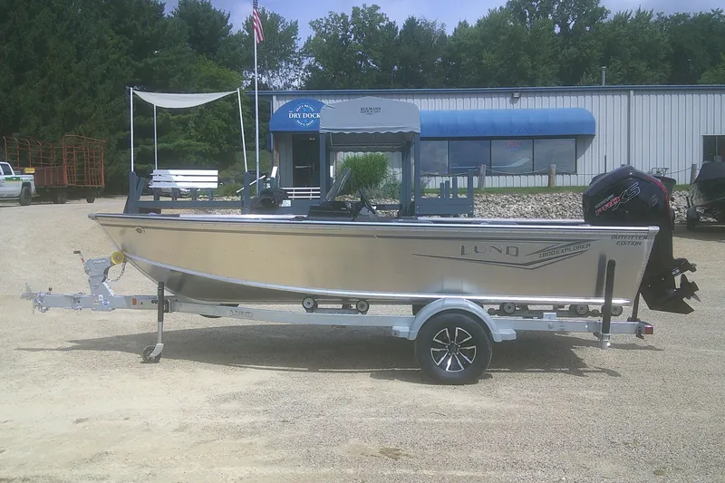 The Image of 2026 Lund 1800 Explorer SS boat on trailer, parked outdoors near a building. - 1