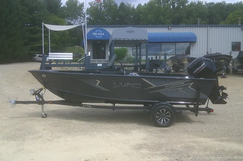 The Image of 2026 Lund 1675 Adventure SS boat on trailer, parked outside a marine shop. - 1