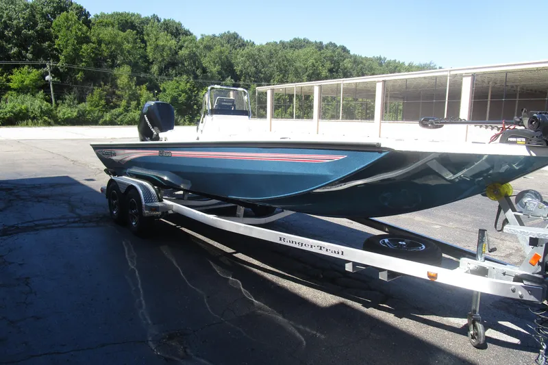 Slide: The Image of 2025 Ranger RB210 boat on trailer, parked outdoors with trees in background. - 6