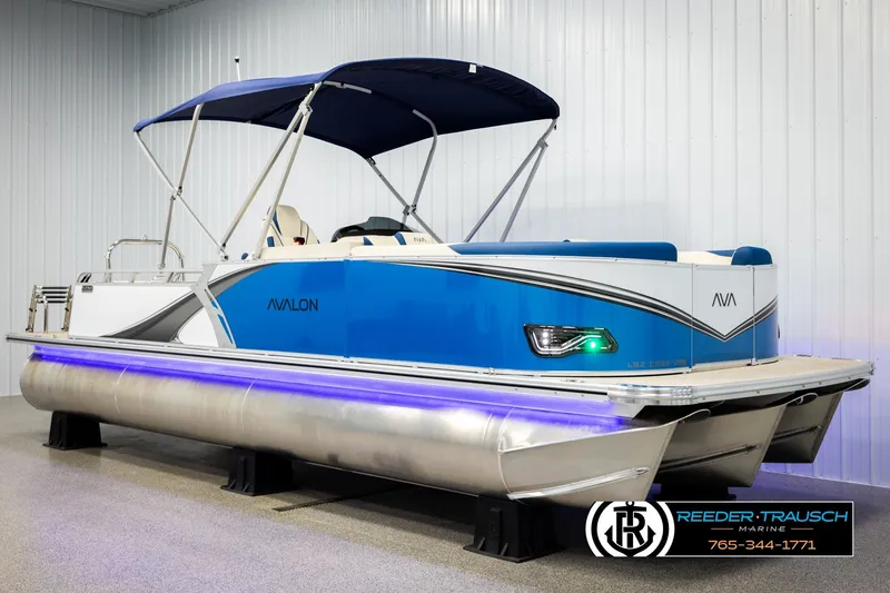 Slide: The Image of 2026 Avalon LSZ VRB pontoon boat with blue canopy and sleek design in showroom. - 3