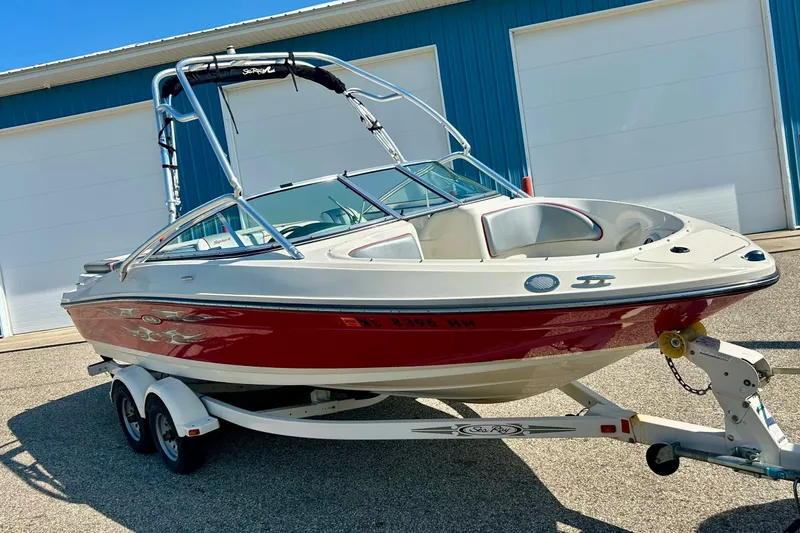 The Image of 2008 Searay 205 SPORT boat on trailer, red and white, parked near blue building. - 1