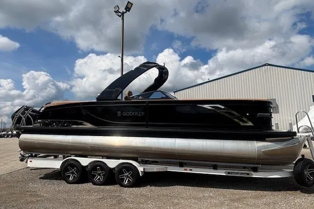 Slide: The Image of 2025 Godfrey San Pan SP2700SBW pontoon boat on trailer, under cloudy sky. - 7