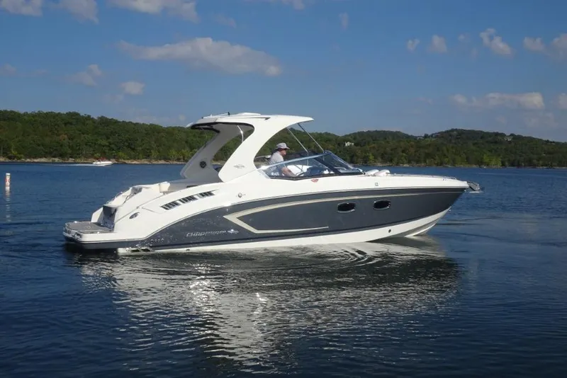 Slide: The Image of 2015 Chaparral 327 SSX boat cruising on a serene lake with forested hills. - 2