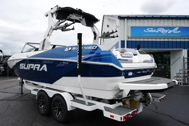 Slide: The Image of 2026 Supra SA boat on trailer outside dealership, featuring blue and white design. - 7