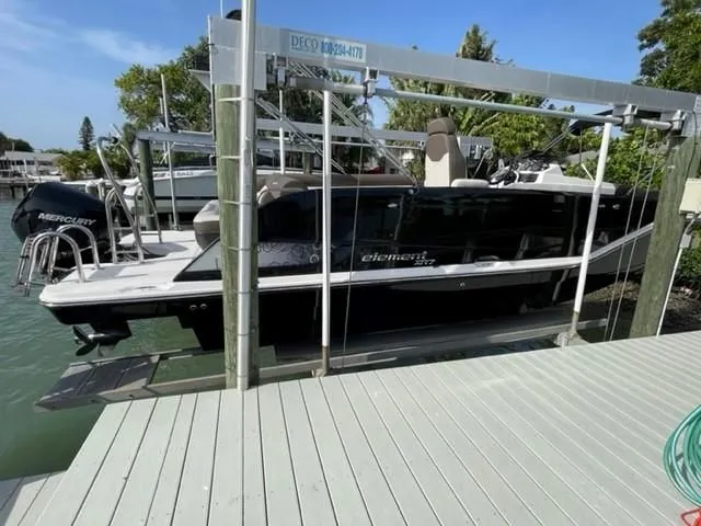 Slide: The Image of 2020 Bayliner Element XR7 boat on lift, docked by water, with trees in background. - 8