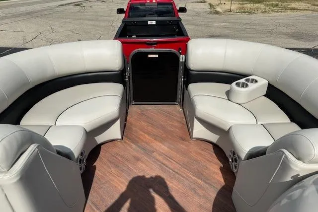 Slide: The Image of 2017 Manitou 23 Oasis boat interior with plush seating and cup holders, parked near a red truck. - 16