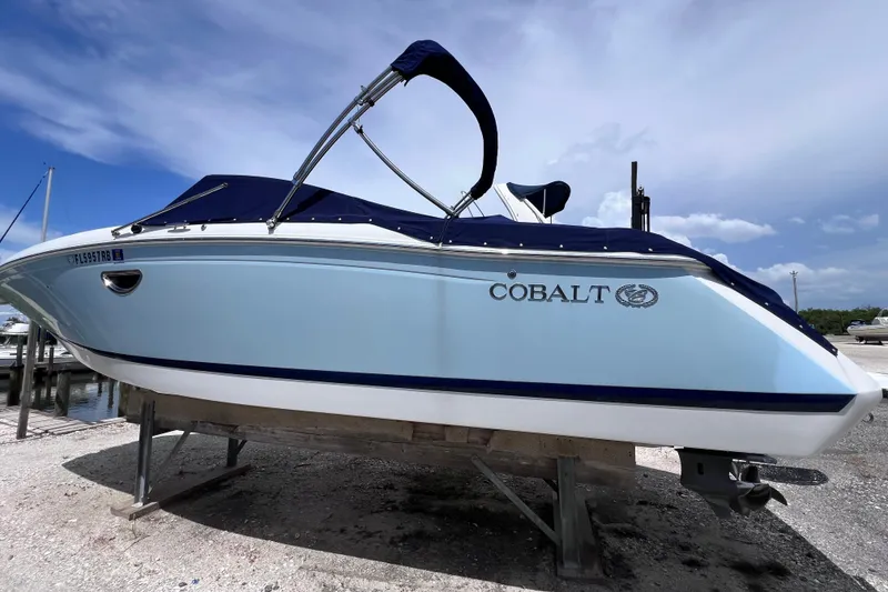 Slide: The Image of 2015 Cobalt 26SD boat with blue cover on a stand, under a clear sky. - 2