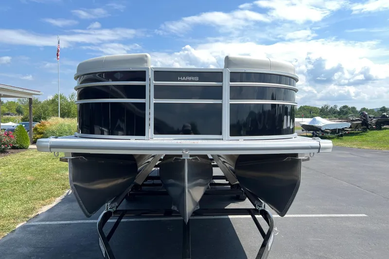 Slide: The Image of 2025 Harris Cruiser 230 pontoon boat on trailer, parked outdoors under a blue sky. - 2