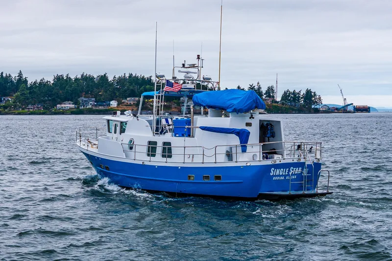 Slide: The Image of Blue and white 1978 Hidden Harbor Custom Trawler on water, with American flag, near forested shoreline. - 8
