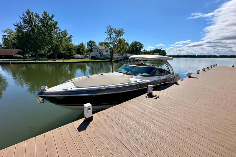 Slide: The Image of 2015 Formula 350 Crossover Bowrider I/O docked on a serene lake under a clear sky. - 2