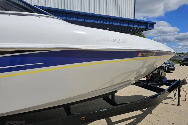 Slide: The Image of 2005 Baja 275 boat on trailer, white with blue and yellow accents, parked outdoors. - 4
