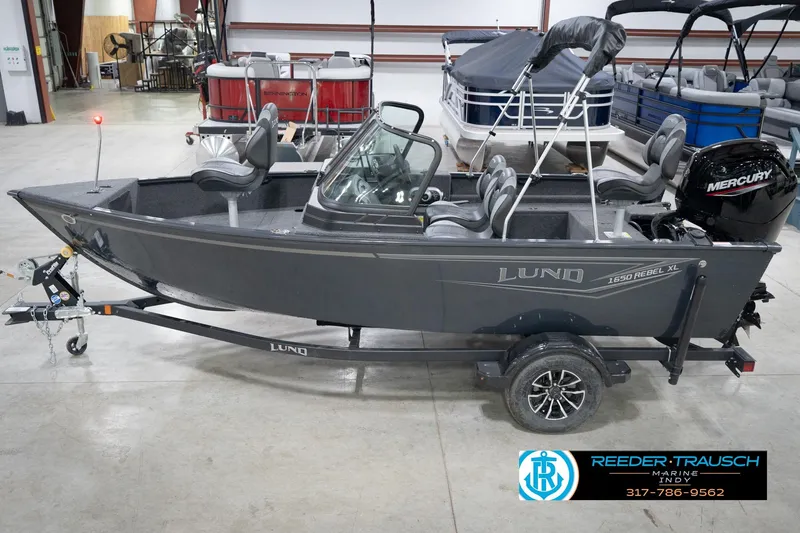 The Image of 2026 Lund 1650 Rebel XL Sport boat in showroom, featuring Mercury engine and trailer. - 0