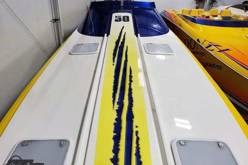 Slide: The Image of 2001 Hustler 50 Monster speedboat with bold yellow and blue design in a showroom. - 25