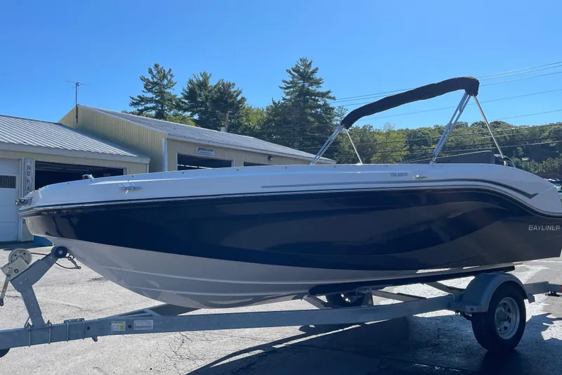 Slide: The Image of 2024 Bayliner DX 2000 boat on trailer, parked outdoors under clear blue sky. - 7