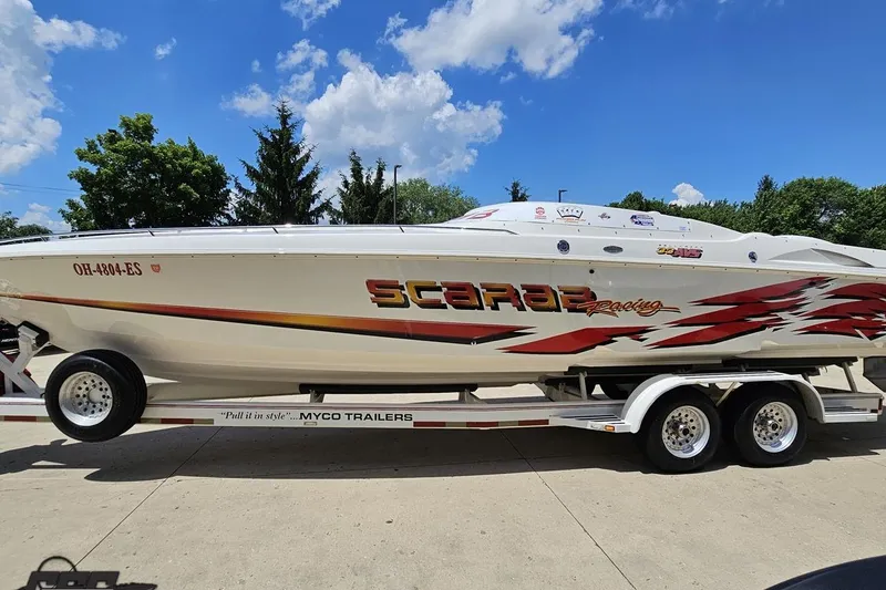 Slide: The Image of 2001 Wellcraft 33 Scarab AVS boat on trailer, vibrant graphics, clear sky background. - 19