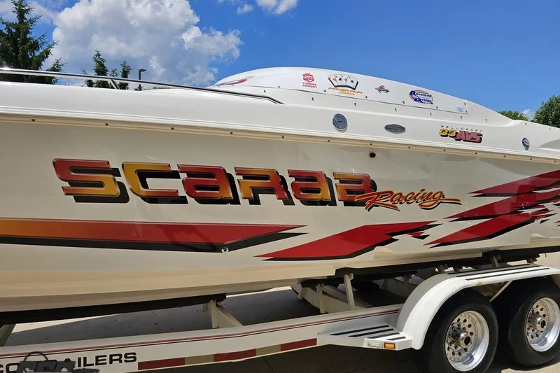 Slide: The Image of 2001 Wellcraft 33 Scarab AVS boat with vibrant racing graphics on a trailer. - 21