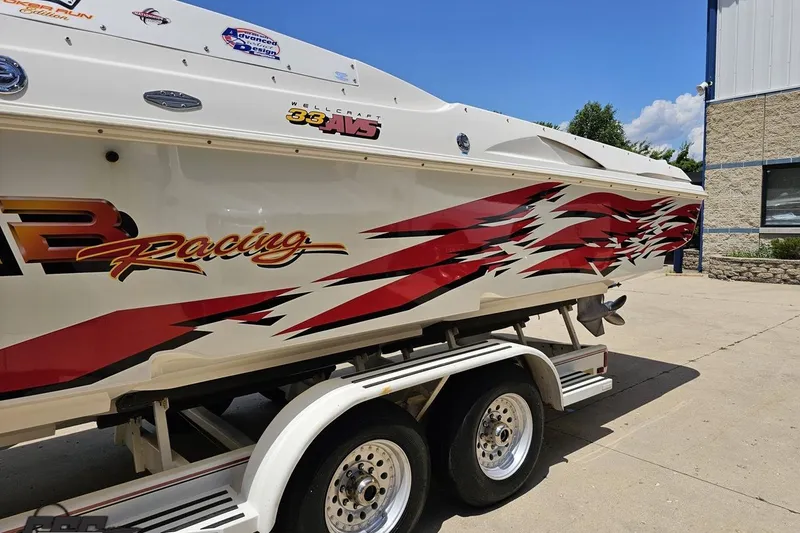 Slide: The Image of 2001 Wellcraft 33 Scarab AVS boat with vibrant racing graphics on a trailer. - 22