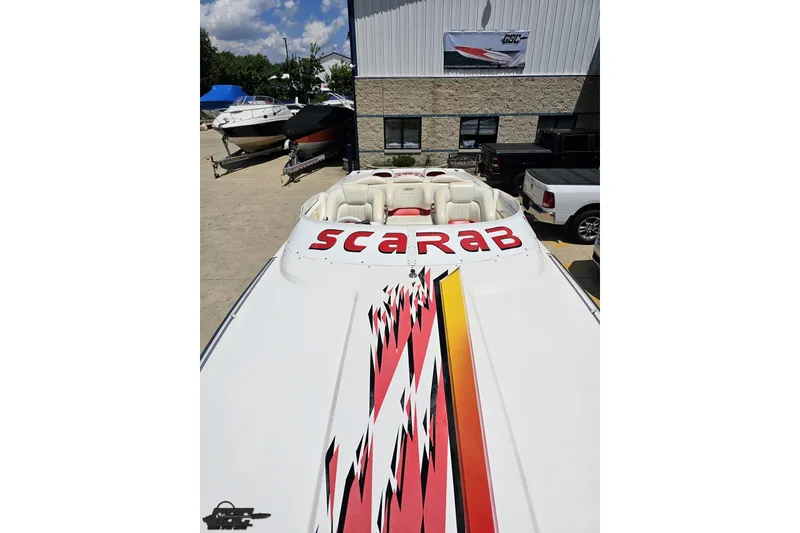 Slide: The Image of 2001 Wellcraft 33 Scarab AVS boat with vibrant graphics, parked outdoors near other boats. - 70