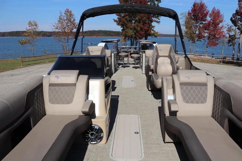 Slide: The Image of 2023 Vanderbilt 700 Twin luxury pontoon boat with plush seating, docked by a scenic lake. - 1