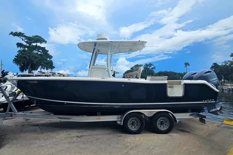 Slide: The Image of 2016 Sea Hunt Gamefish 25 boat on trailer, parked near water under a blue sky. - 7