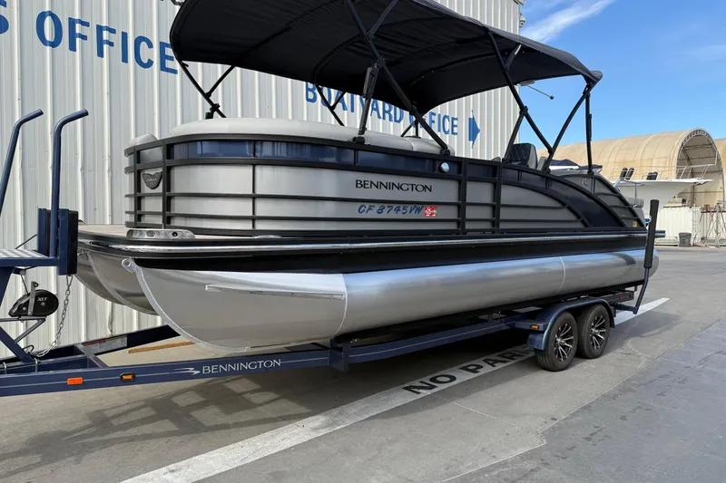 Slide: The Image of 2024 Bennington 23 RSB pontoon boat on trailer, parked near a building. - 1