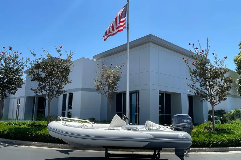 Slide: The Image of 2007 Zodiac Yachtline Deluxe 420 boat on trailer, parked near modern building with American flag. - 19