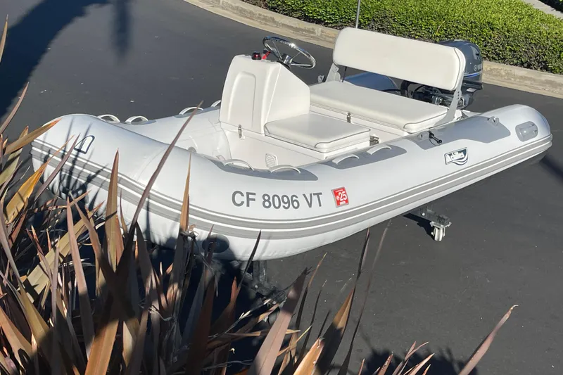 Slide: The Image of 2020 Achilles HB-315DX inflatable boat with motor, parked on pavement, surrounded by plants. - 11