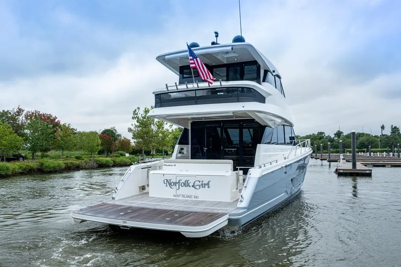 Slide: The Image of 2023 Maritimo M55 yacht docked, rear view with American flag, lush greenery in background. - 119