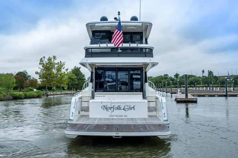 Slide: The Image of 2023 Maritimo M55 yacht docked, rear view with American flag, lush greenery in background. - 120