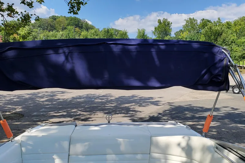 Slide: The Image of 2006 Cobalt 246 boat with blue bimini top, parked under trees on a sunny day. - 35