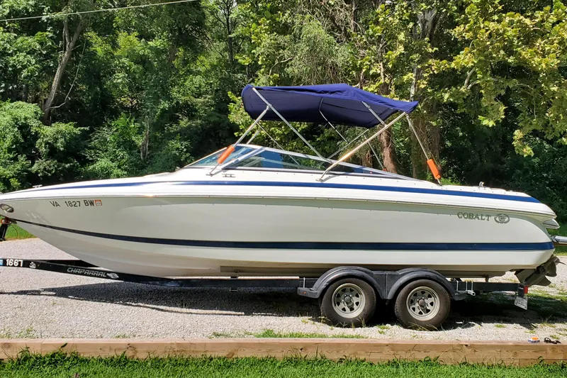 Slide: The Image of 2006 Cobalt 246 boat on trailer, parked outdoors with lush green background. - 39