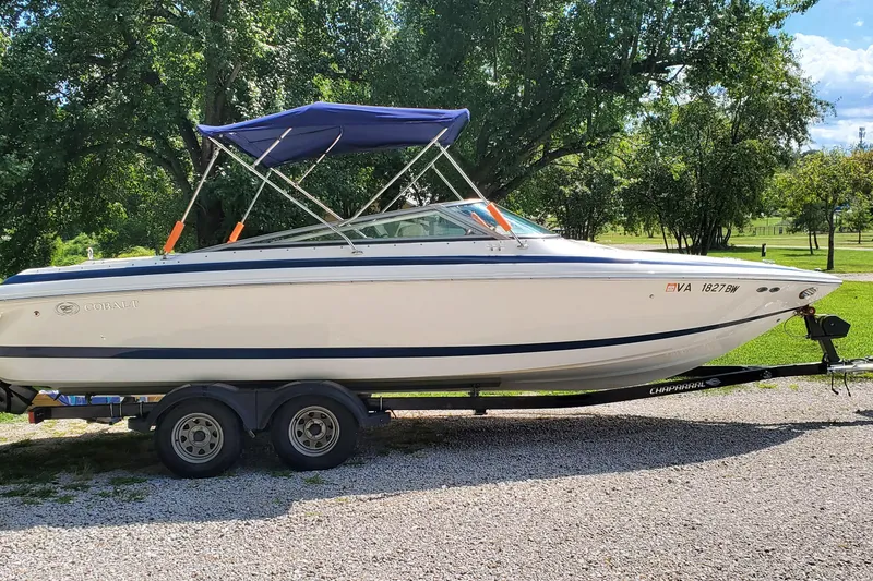 Slide: The Image of 2006 Cobalt 246 boat on trailer with blue canopy, parked on gravel, surrounded by trees. - 41
