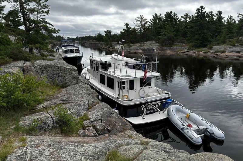 Slide: The Image of American Tug 34 Pilothouse 2005 moored by rocky shoreline with inflatable boat. - 12