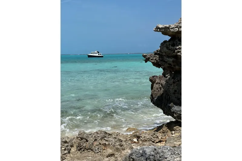 Slide: The Image of American Tug 34 Pilothouse (2005) on turquoise sea near rocky shore. - 121