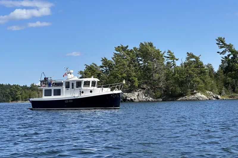 Slide: The Image of 2005 American Tug 34 Pilothouse cruising near a forested island on a sunny day. - 123