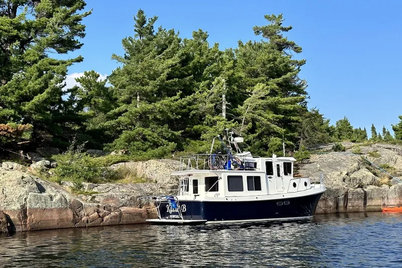 Slide: The Image of 2005 American Tug 34 Pilothouse moored by rocky shoreline with lush trees. - 124