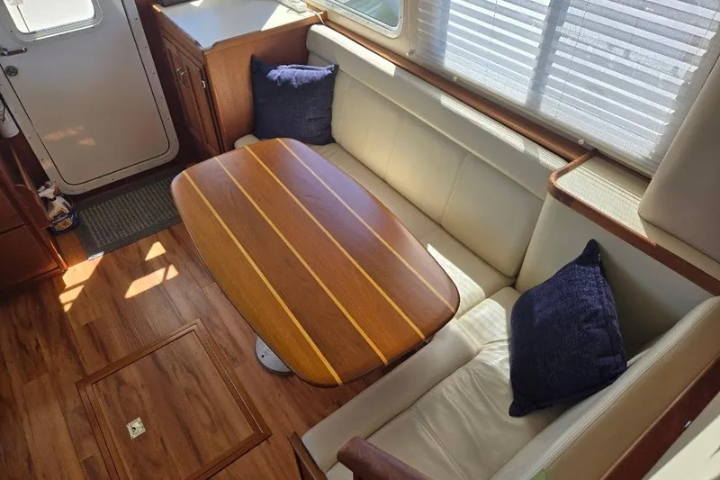 Slide: The Image of 2005 American Tug 34 Pilothouse interior with wooden table, cushioned seating, and blue pillows. - 16