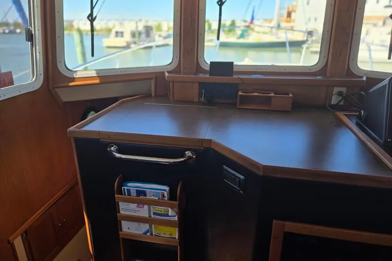 Slide: The Image of Pilothouse interior of 2005 American Tug 34, featuring navigation desk and windows with marina view. - 60