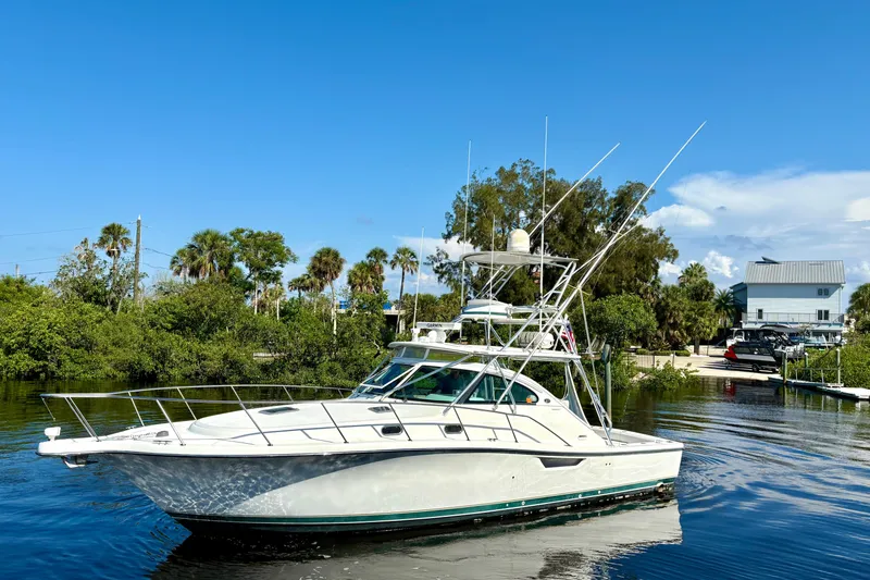 The Image of 2002 Pursuit 3800 Express yacht on calm water, surrounded by lush greenery and clear blue sky. - 1