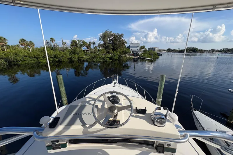 Slide: The Image of 2002 Pursuit 3800 Express boat helm with Garmin navigation, docked near lush greenery. - 22