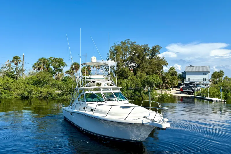 Slide: The Image of 2002 Pursuit 3800 Express yacht on calm water, surrounded by lush greenery and clear blue sky. - 3