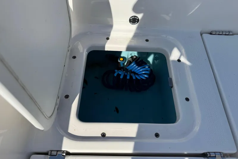 Slide: The Image of Open storage compartment on 2018 Yamaha Boats 210 FSH, featuring coiled blue hose. - 22