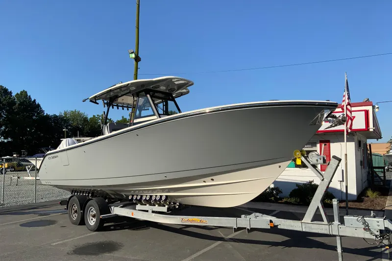 Slide: The Image of 2026 Cobia 305 Center Console boat on trailer, parked outdoors under clear blue sky. - 2