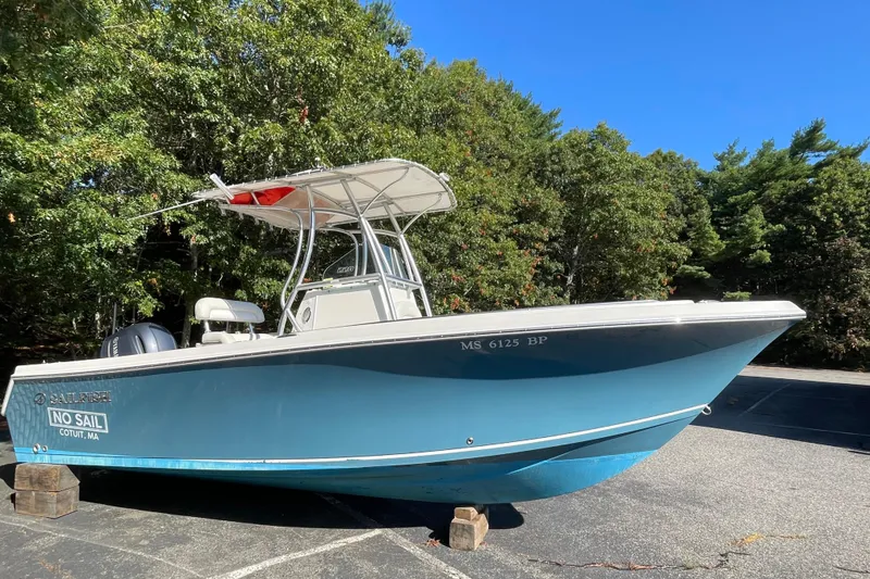 Slide: The Image of 2014 Sailfish 220 CC boat on land, surrounded by trees, under clear blue sky. - 2