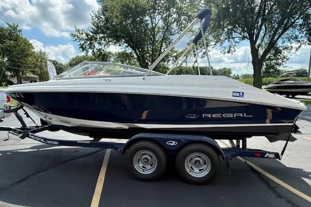 Slide: The Image of 2012 Regal 2000 Bowrider boat on trailer, parked outdoors under a clear sky. - 3