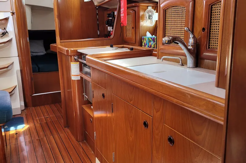 Slide: The Image of Interior of 1999 Beneteau Oceanis 351 yacht, featuring wooden cabinetry and compact kitchen area. - 33