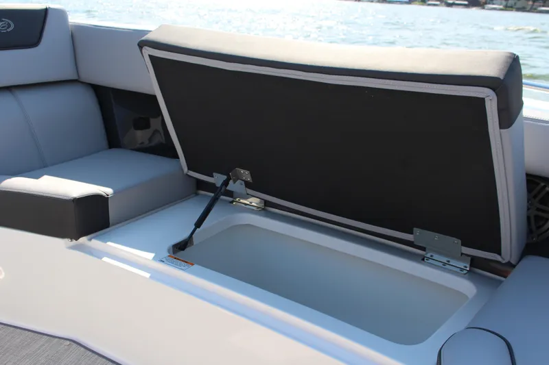 Slide: The Image of 2025 Cobalt R35 boat storage compartment with open cushioned seat, lake view in background. - 85