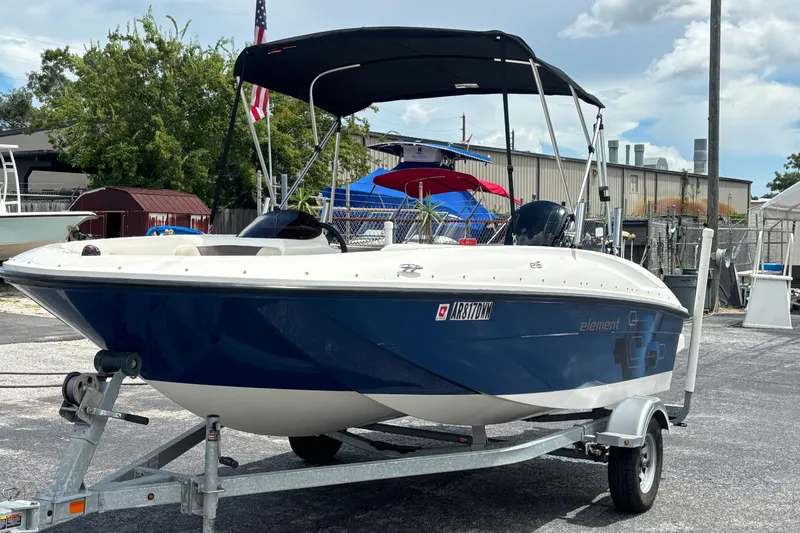 Slide: The Image of 2018 Bayliner Element E16 boat on trailer, parked outdoors under a cloudy sky. - 2