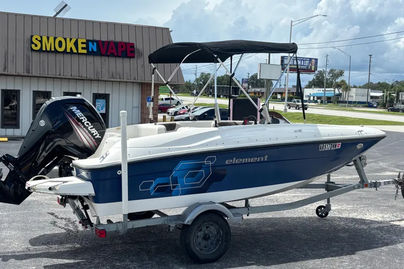 Slide: The Image of 2018 Bayliner Element E16 boat on trailer near a store, featuring a Mercury engine. - 6