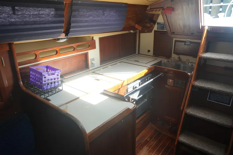 Slide: The Image of 1984 Ericson 38 yacht interior with wooden cabinetry, compact kitchen, and stairs leading to deck. - 18